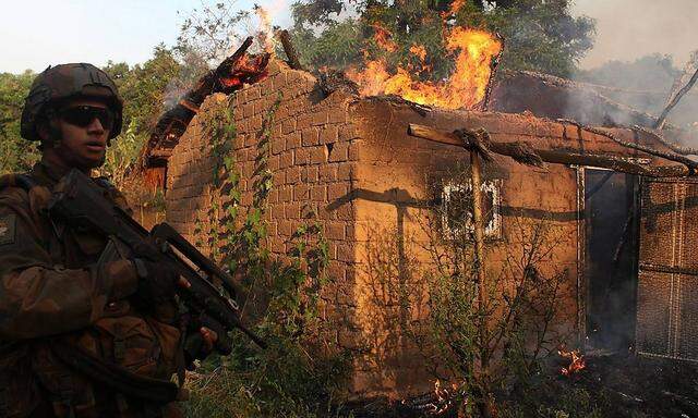 A French soldier patrols past a house on fire at a village in Bossangoa