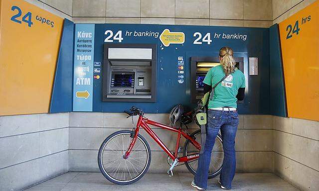 A woman withdraws money from an ATM outside a Bank of Cyprus branch before it opens in Nicosia