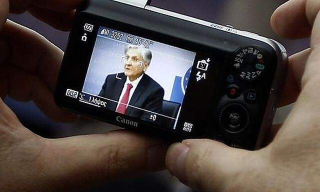 A reporter takes a photograph of Trichet, President of the European Central Bank (ECB) as he answers 