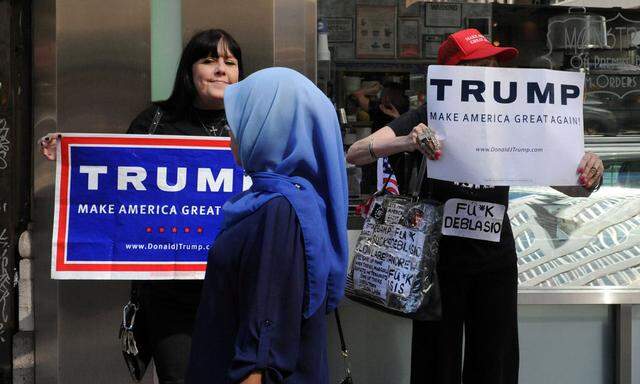 A woman wearing a Muslim headscarf walks past people holding U.S. Republican presidential nominee Donald Trump signs before the annual Muslim Day Parade in the Manhattan borough of New York City