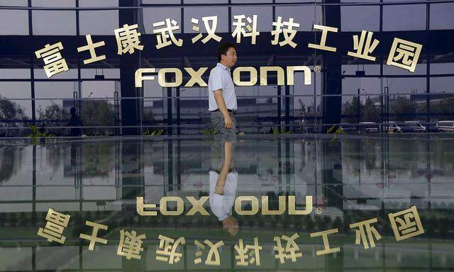File photo of a man walking past a logo of a Foxconn factory in Wuhan