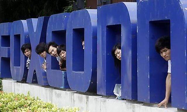 Workers look on from a Foxconn logo near the gate of a Foxconn factory in the township of Longhua