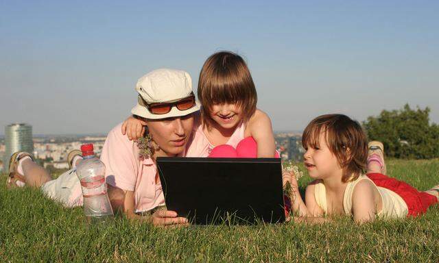 Frau und Kinder mit Notebook auf einer Wiese