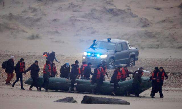 Diese Aufnahme zeigt Migranten, die an der französischen Küste ein Gummiboot zum Wasser schleppen, um damit nach England zu fahren. Die Polizei schaut zu. 
