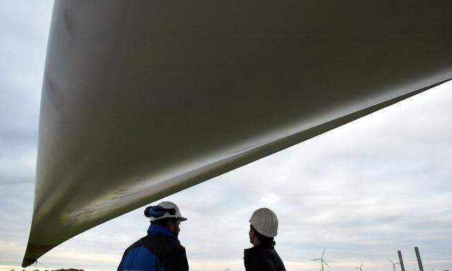 Technicians stand under a rotor wing of a giant wind generator during its assembly on a construction..