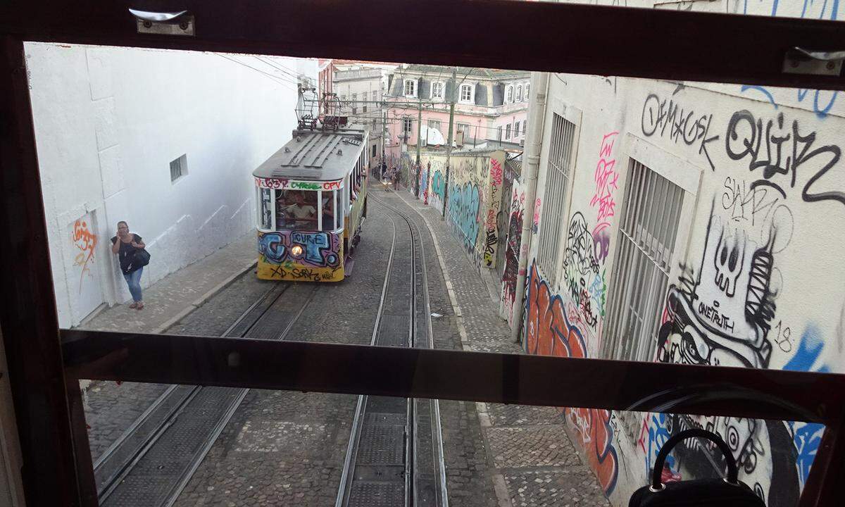 Das ist keine reguläre Straßenbahn, sondern nominell ein Aufzug („elevador“), real eine Standseilbahn, der berühmte Elevador da Glória, der die Baixa (Unterstadt) mit dem Bairro Alto (Ausgehviertel und auch Oberstadt) verbindet. Dabei überwindet er auf steilem Gelände auf 265 Metern 48 Höhenmeter. Seit 1885, ursprünglich mit Wasserballast-Antrieb und abends mit Kerzen beleuchtet, fahren zwei Waggons auf und ab. Im 21. Jahrhundert bilden sich oft lange Schlangen, der Touristenandrang verdrängt viele Einheimische aus ihrem angestammten Verkehrsmittel.