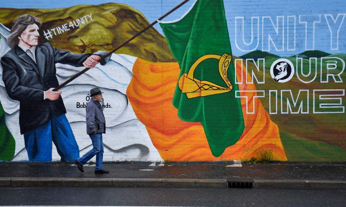A man walks past a mural, in Belfast