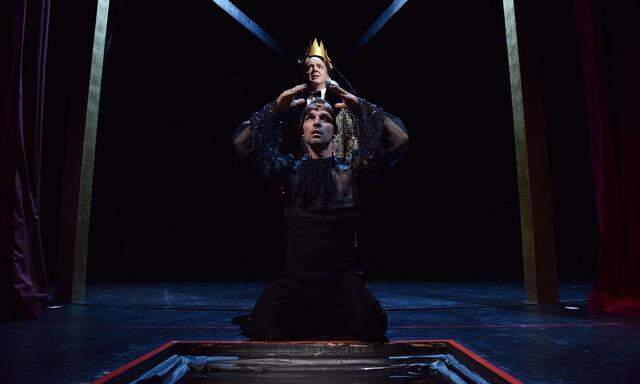 Hamlet (Tim Breyvogel) kniet mit großer Geste, dahinter steht sein böser Onkel Claudius (Michael Scherff) mit der Krone, die ihm die Gattin aufsetzt.
