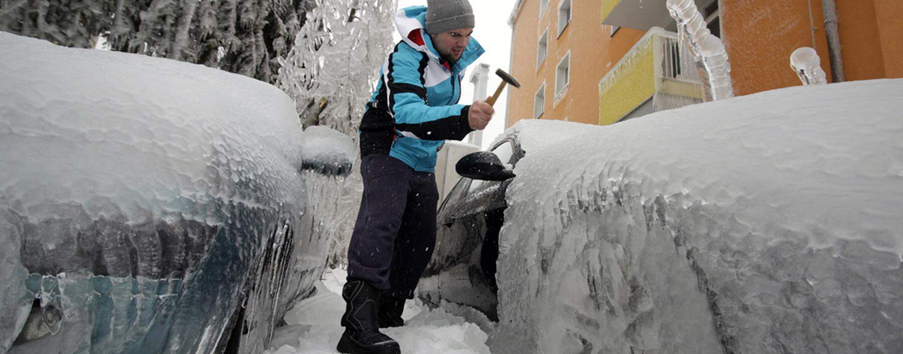 Man removes ice from an ice-covered car with a hammer in Postojna