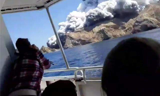 People on a boat react as smoke billows from the volcanic eruption of Whakaari, also known as White Island