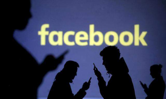FILE PHOTO: Silhouettes of mobile users are seen next to a screen projection of Facebook logo