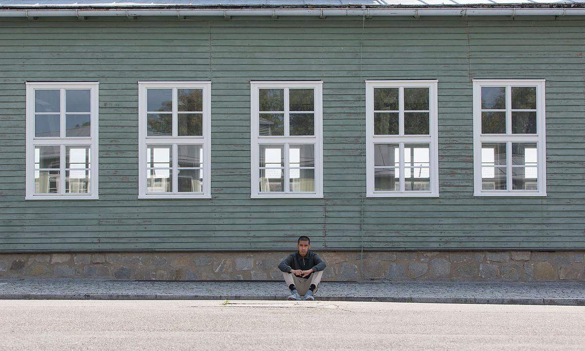 Ein muslimischer Jugendlicher sitzt am ehemaligen Appellplatz im Schatten einer der noch wenigen erhaltenen Barracken.