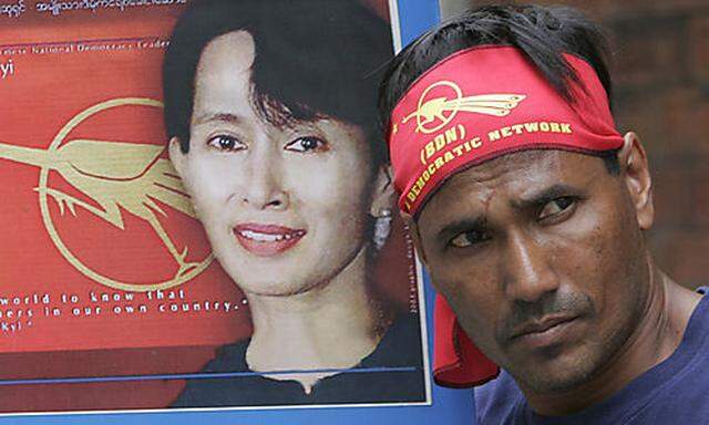 A Myanmar activist stands next to posters of pro-democracy leader Aung San Suu Kyi during a protest, 