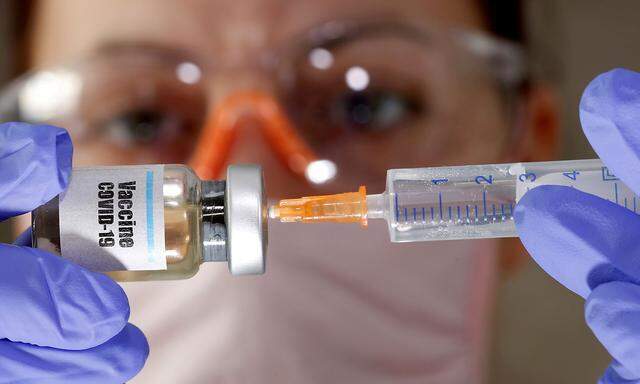 FILE PHOTO: A woman holds a small bottle labeled with a 'Vaccine COVID-19' sticker and a medical syringe in this illustration