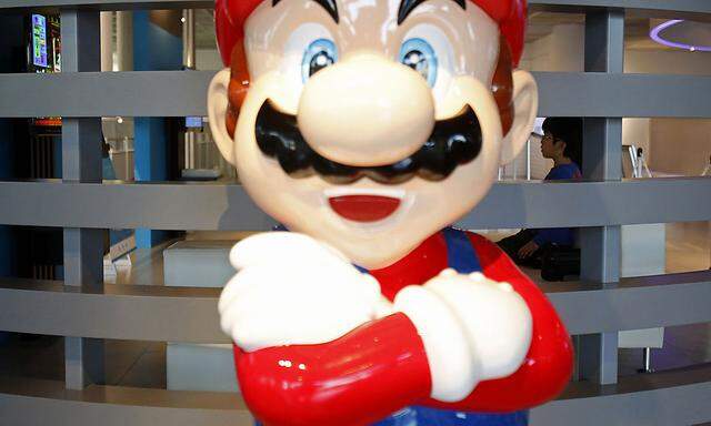 A boy seated behind a Super Mario figure watches a monitor displaying Nintendo Co Ltd´s Wii U game console at its showroom in Tokyo