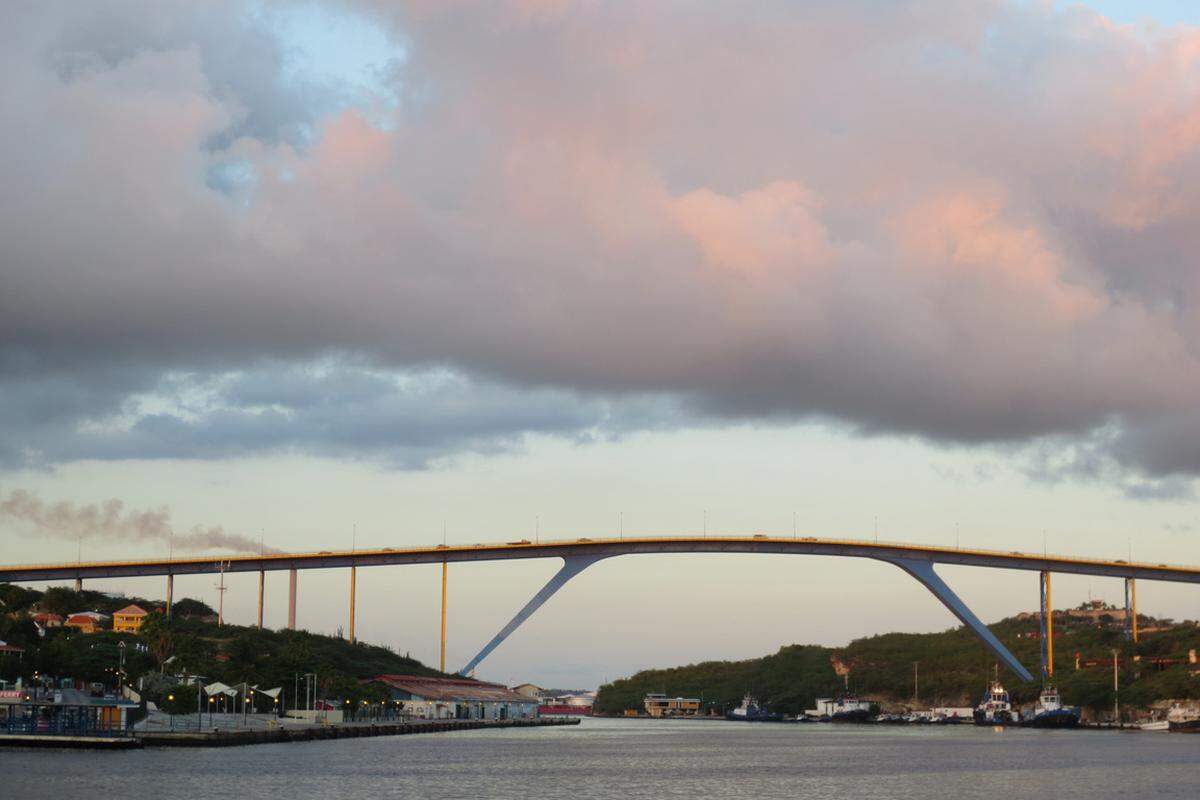 Hier schlägt das wirtschaftliche Herz von Willemstad, der größten Stadt der niederländischen Überseegebiete und der Hauptstadt Curaçaos. Durch den Sint Annabaai fahren die Schiffe in den natürlichen Hafen Schottegat, oben drüber gleiten die Autos über die Queen Juliana Bridge – die größte, aber nur zweitpopulärste Brücke der Insel …