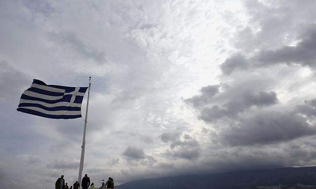 Tourists stand under a Greek national flag atop Acropolis hill in Athens