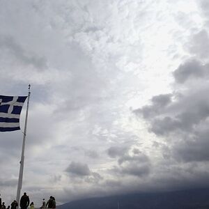 Tourists stand under a Greek national flag atop Acropolis hill in Athens