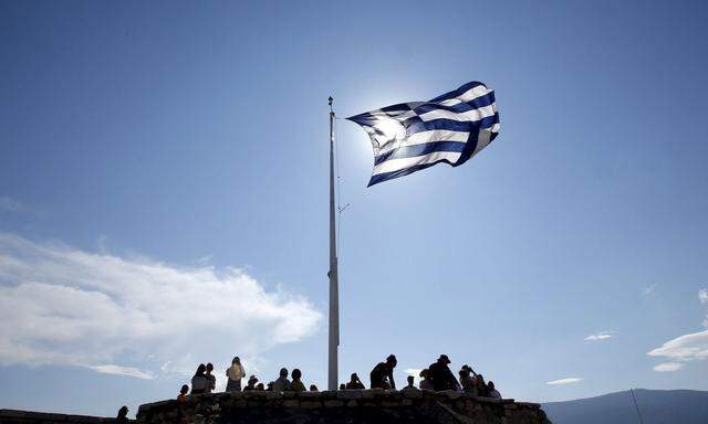 A Greek flag flutters as tourists visit the Acropolis hill archaeological site in Athens