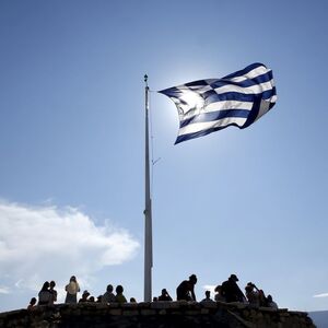 A Greek flag flutters as tourists visit the Acropolis hill archaeological site in Athens