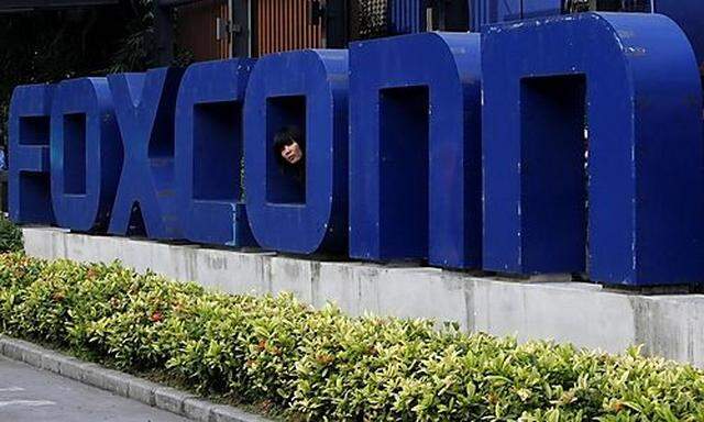 A worker looks out through the logo at the entrance of the Foxconn complex in the southern Chinese ci