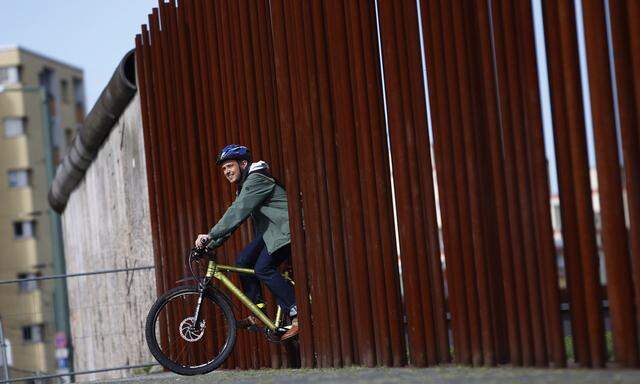 A man rides his bike through gap in row of metal rods that delineates line along which Berlin Wall used to run at Berlin Wall memorial site in Berlin