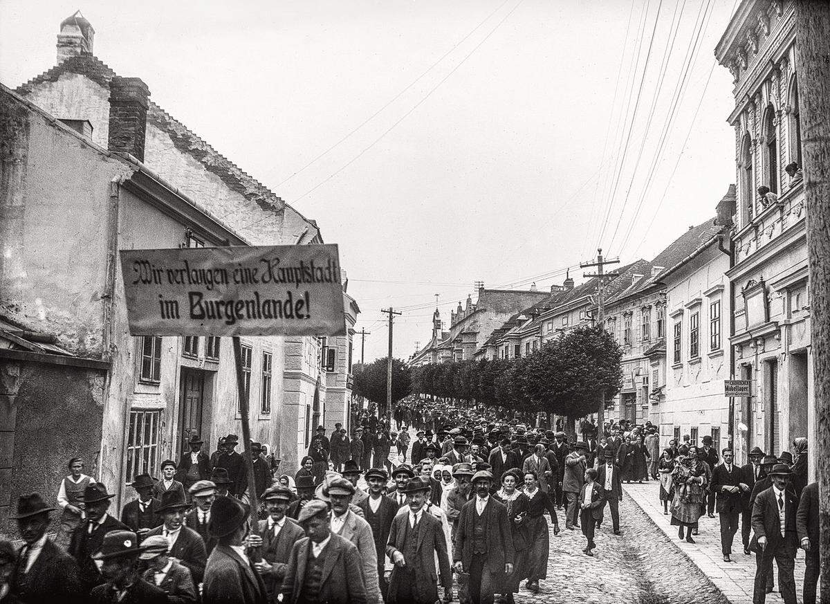 Um 1923/25: Demonstration durch die Hauptstraße in Eisenstadt. "Wir verlangen eine Hauptstadt im Burgenlande!" lautete die Forderung. Ursprünglich war Ödenburg (Sopron) als Landeshauptstadt vorgesehen gewesen. Stattdessen wurde Eisenstadt 1925 zum Sitz der burgenländischen Landesregierung. Erst 1965 verankerte Eisenstadt den Status der Landeshauptstadt.  