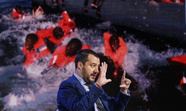 Italiens Innenminister, Matteo Salvini, hier in einer TV-Show, die im Hintergrund Bilder von Bootsflüchtlingen zeigt. Der Lega-Politiker fordert bei der Migration mehr Solidarität von der EU. 