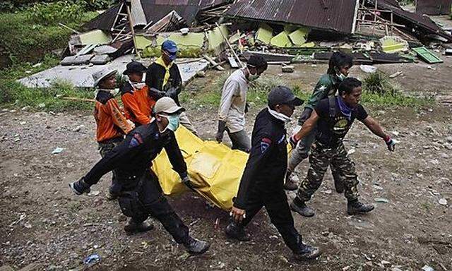 Indonesian rescue volunteers carry a body past a destroyed house in an area severely hit by landslide