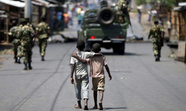 Boys walk behind patrolling soldiers in Bujumbura