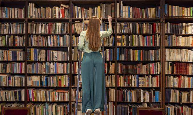 Young woman standing on ladder while searching book in library model released Symbolfoto property released VEGF04390