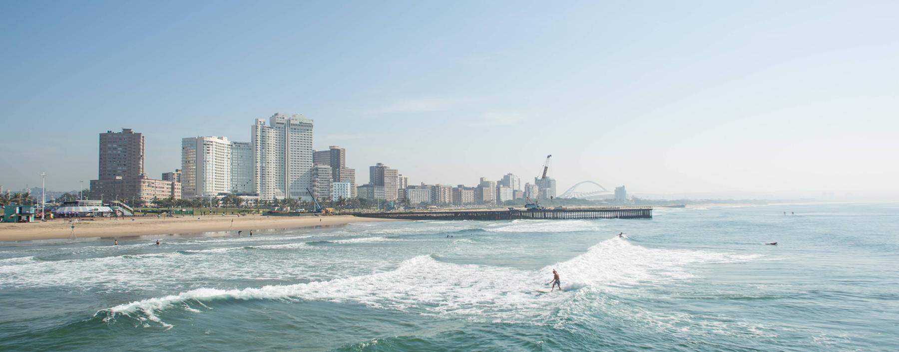 Surfers riding waves near pier on Golden Mile with skyline of Durban South Africa Durban KwaZulu N