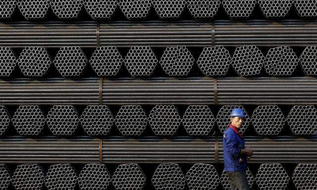 File photo of a worker walks past a pile of steel pipe products at the yard of Youfa steel pipe plant in Tangshan in China's Hebei Province