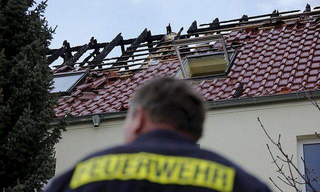 A firefighter stands in front of a building damaged by a fire, which will be used as an asylum seekers home, in Troeglitz