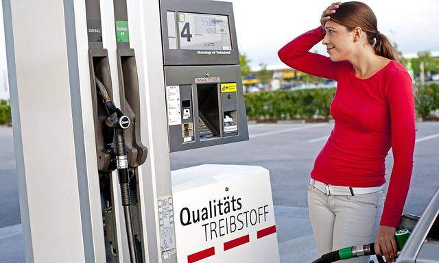 junge Frau steht an der Zapfsaeule einer Tankstelle und haelt sich mit Blick auf den Spritpreis fass