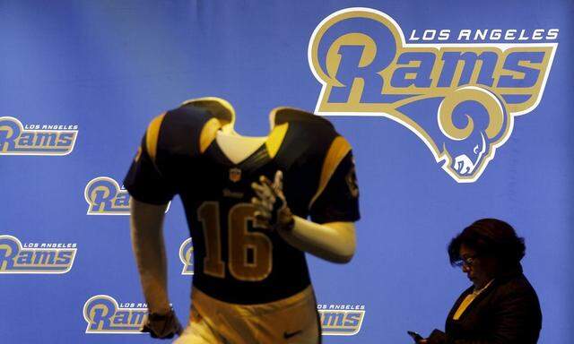 A women looks at her phone as she walks past a Los Angeles Rams mannequin at the NFL Experience