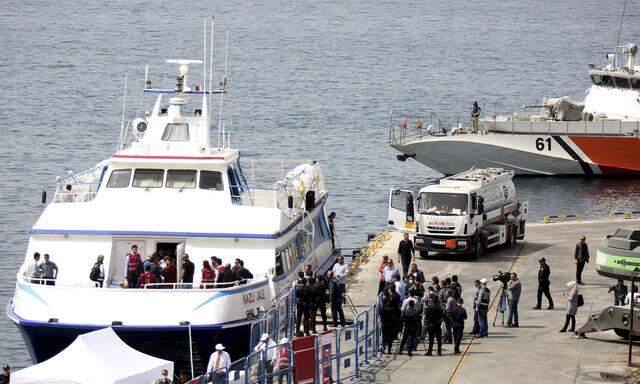 Migrants are escorted by police officers as they disembark from a ferry at a port in the Turkish coastal town of Dikili