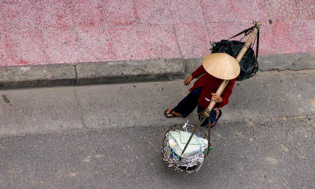 Ein Vietnamese mit traditionellem kegelförmigen Hut trägt zwei Warenkörbe an einer Bambusstange. Das Land produziert freilich längst auch Hightech.