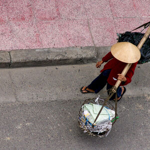 Ein Vietnamese mit traditionellem kegelförmigen Hut trägt zwei Warenkörbe an einer Bambusstange. Das Land produziert freilich längst auch Hightech.