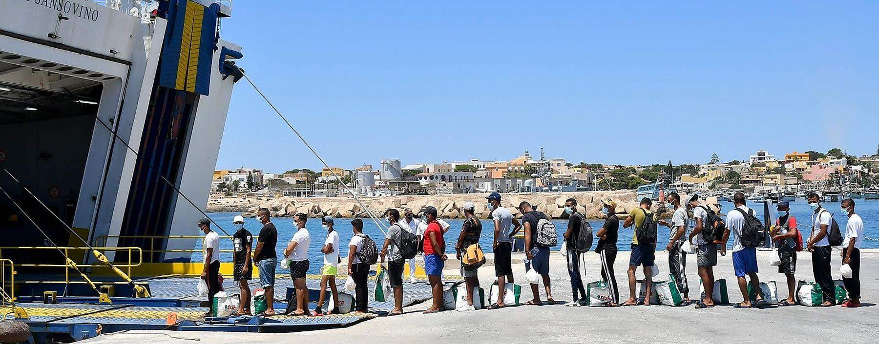 Migranten und Flüchtlinge stellen sich an, um von den Behörden per Fähre von Lampedusa weiter nach Sizilien gebracht zu werden. 