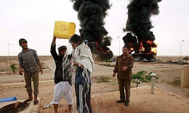 A man douses water to a friend before retrieving a dead person near the site of burning tanks after a