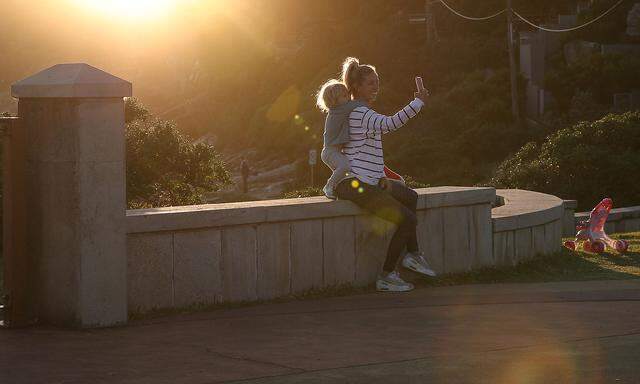 A woman and child take a selfie during sunset at the coast in Sydney