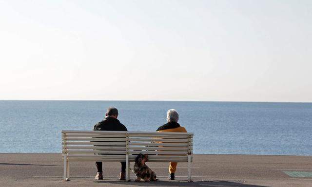 Elderly people sit on a bench to take in the sun along the Promenade Des Anglais in Nice
