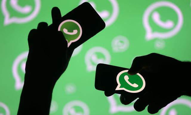 Men pose with smartphones in front of displayed Whatsapp logo in this illustration
