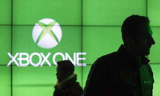 People walk in front of a screen advertising the Xbox One at an event celebrating the console´s midnight launch in New York
