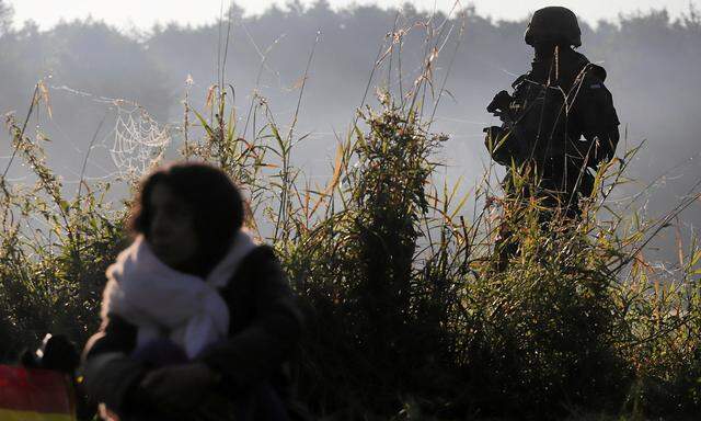 Polish servicemen and border patrol officers guard a group of migrants stranded on the border between Belarus and Poland near Usnarz Gorny