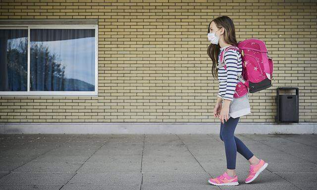 Girl wearing mask and schoolbag walking along building