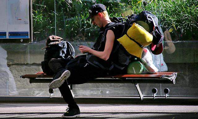 A foreign backpacker sits at a bus stop with his belongings in central Sydney, Australia