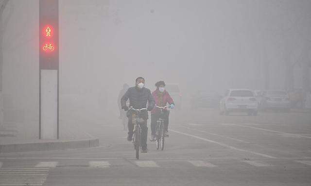 People wearing masks ride bicycles across a street in smog in Liaocheng
