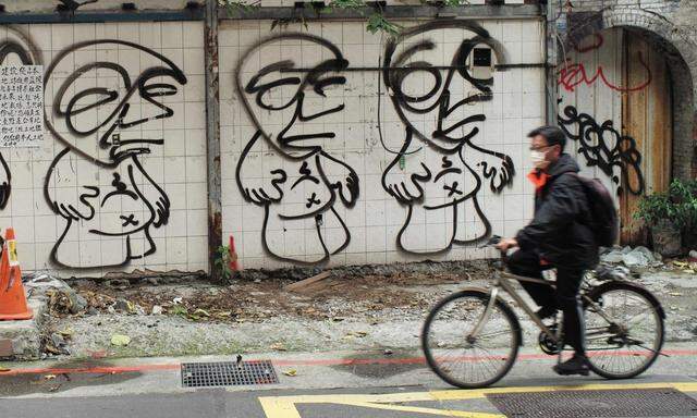Ein Mann fährt mit dem Fahrrad an einer mit Graffiti beschmierten Wand in Taipeh vorbei